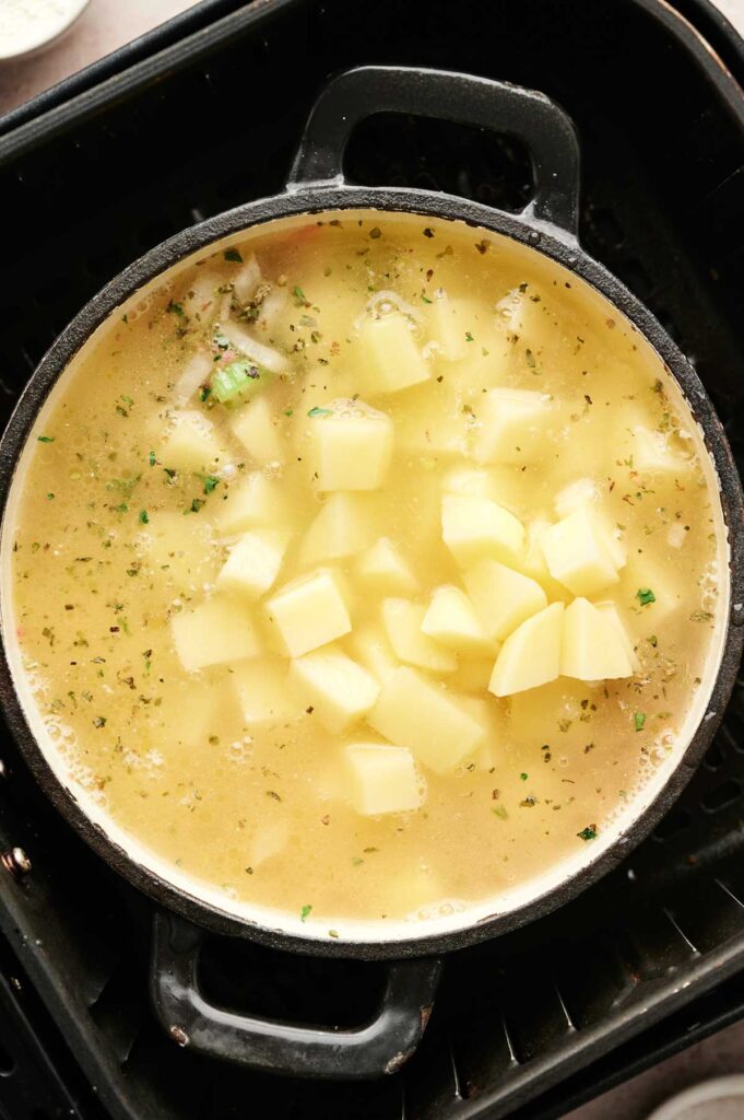 A pot of Air Fryer Cheeseburger Soup with diced potatoes and herbs simmering in a light broth, viewed from above.