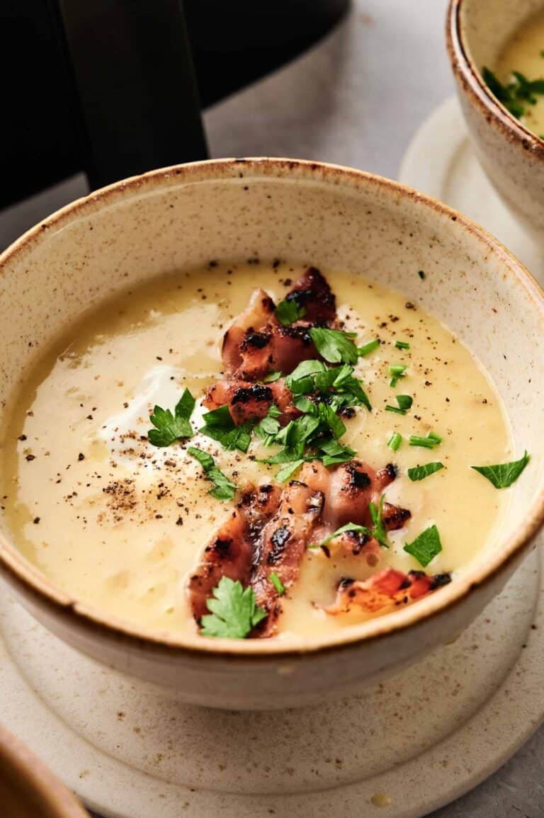 A bowl of creamy Air Fryer Potato Soup topped with grilled bacon strips, chopped parsley, black pepper, and a dollop of sour cream.