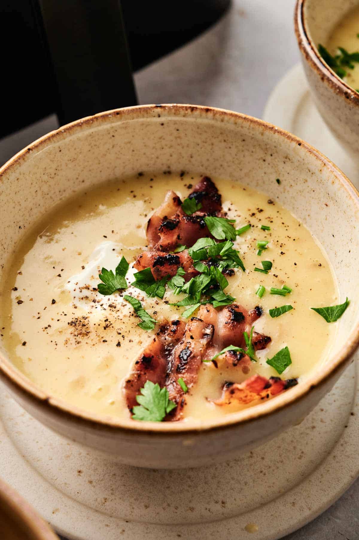 A bowl of creamy Air Fryer Potato Soup topped with grilled bacon strips, chopped parsley, black pepper, and a dollop of sour cream.