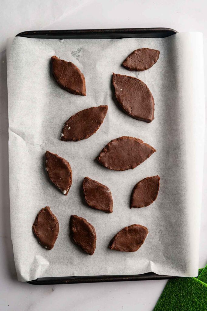 Unbaked chocolate football-shaped cookies arranged on a parchment-lined baking sheet