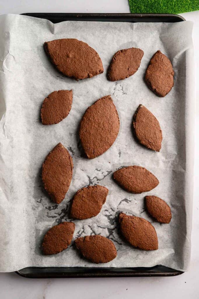 A baking sheet lined with parchment paper holds twelve American Football-Shaped Cookies, each crafted from rich chocolate dough.