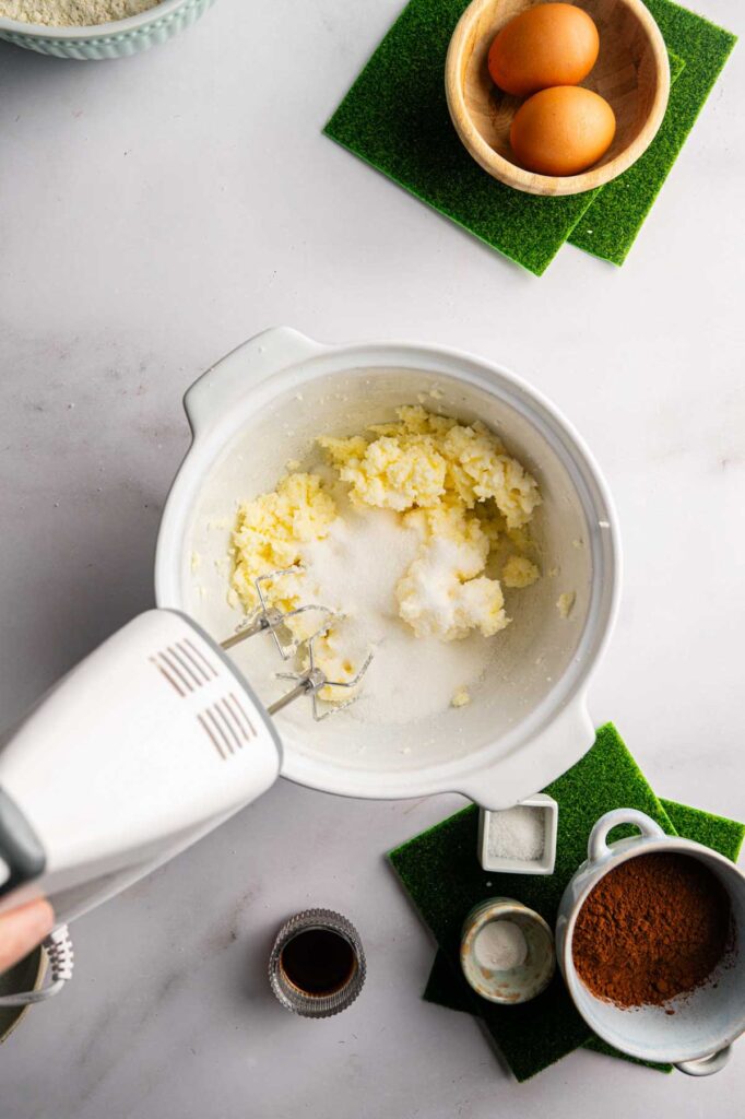 Creaming butter and sugar together in a white mixing bowl with a hand mixer