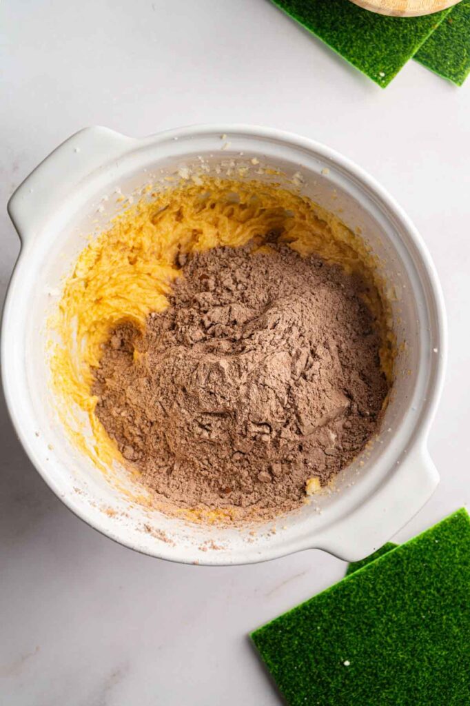 Dry cocoa flour mixture being added into creamed butter in a white mixing bowl