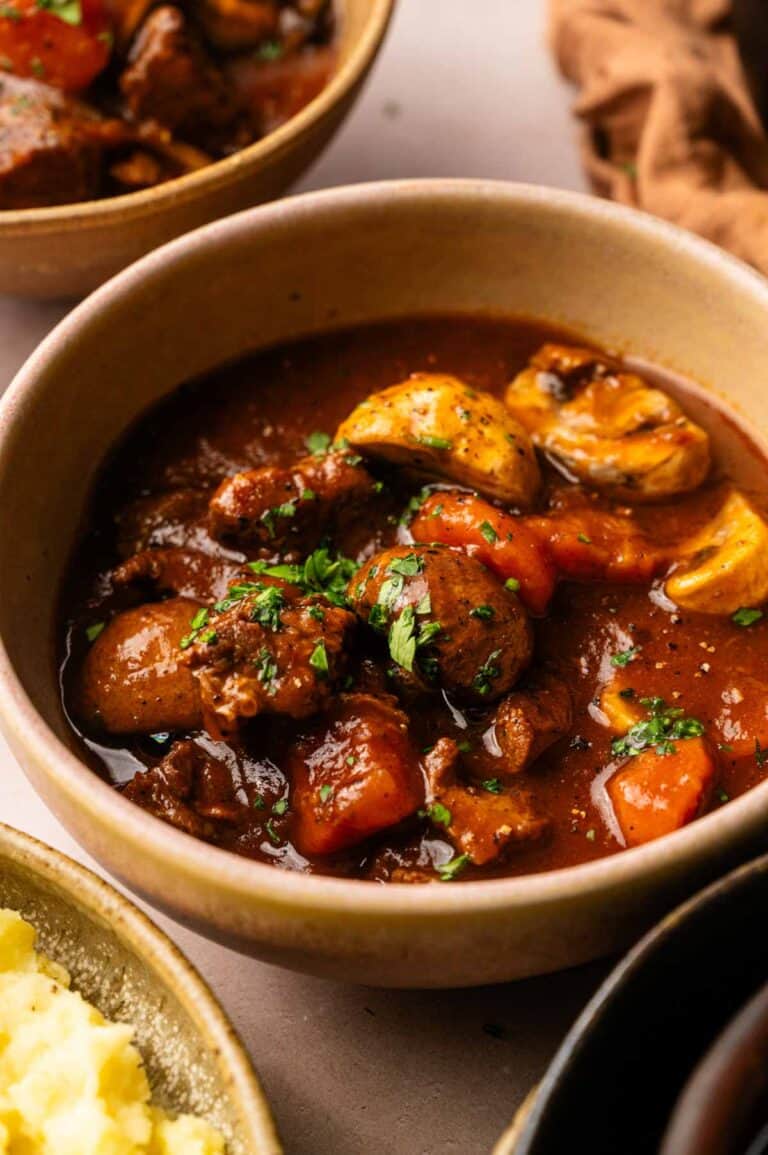 A bowl of Beef and Guinness Stew with tender chunks of beef, carrots, potatoes, mushrooms, and a rich brown broth, garnished with chopped parsley.