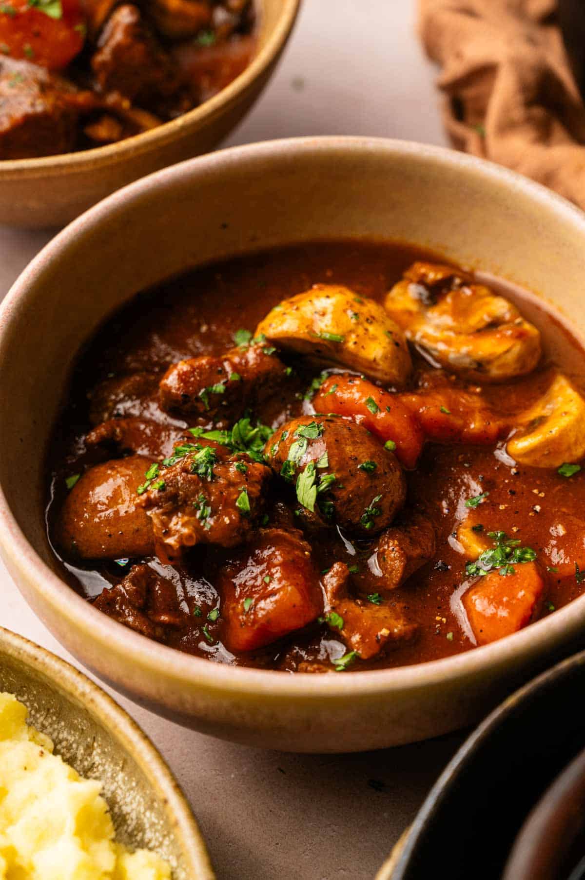 A bowl of Beef and Guinness Stew with tender chunks of beef, carrots, potatoes, mushrooms, and a rich brown broth, garnished with chopped parsley.