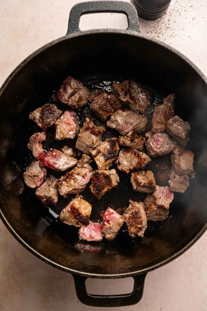 Chunks of beef sizzle in a black cast iron pot, some browned and others still pink&mdash;the perfect start to a hearty Beef and Guinness Stew.