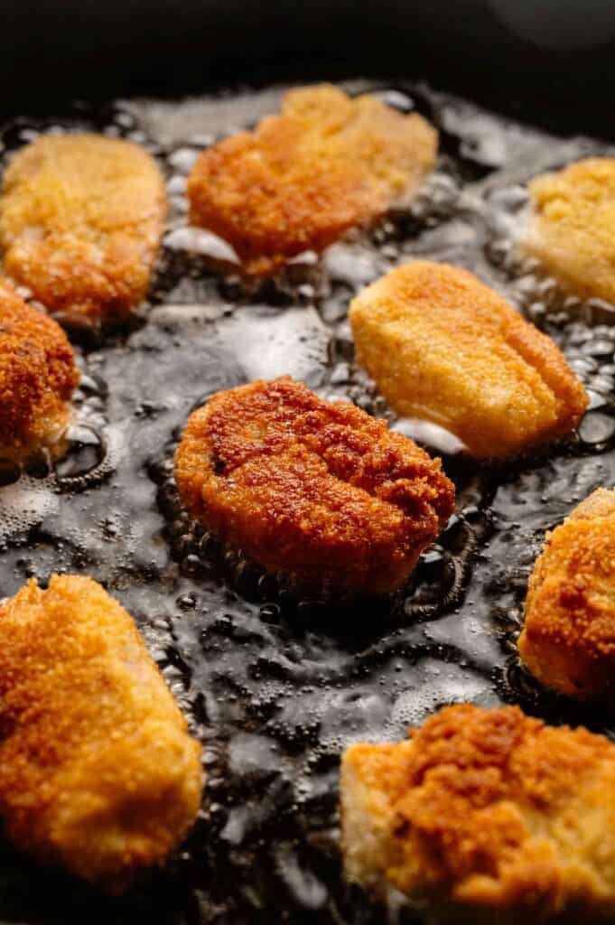 Ham croquettes frying in sizzling oil in a pan, showcasing a golden-brown, crispy coating.