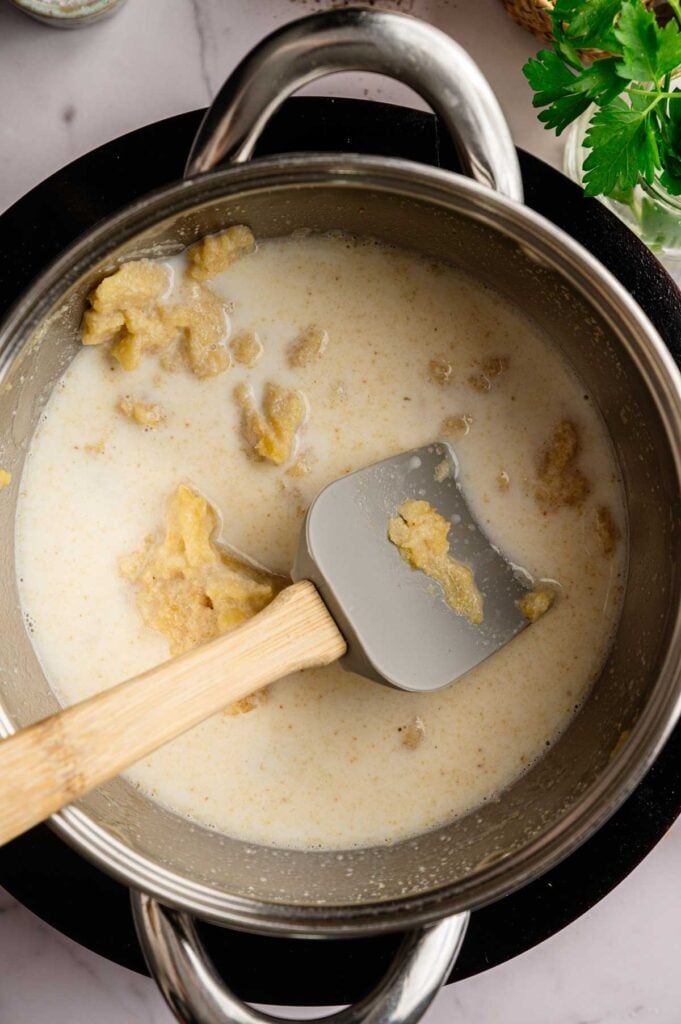 A saucepan containing a thick, beige mixture being stirred with a spatula, likely in the process of cooking or mixing ingredients for Ham Croquettes.