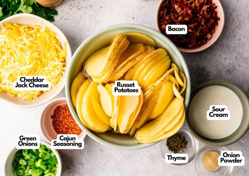 Top-down view of labeled bowls containing ingredients for Irish Nachos, including cheddar jack cheese, green onions, Cajun seasoning, russet potatoes, thyme, bacon, sour cream, and onion powder on a light surface.