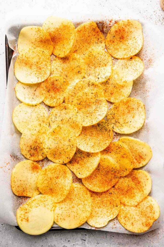 Sliced potatoes arranged on a parchment-lined baking sheet, sprinkled with red and green spices, these Irish Nachos offer a flavorful twist on a classic favorite.