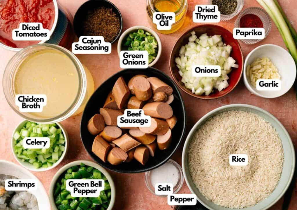 Assorted labeled ingredients for a Jambalaya rice dish, including beef sausage, shrimps, rice, diced tomatoes, vegetables, seasonings, spices, and olive oil, arranged on a countertop.