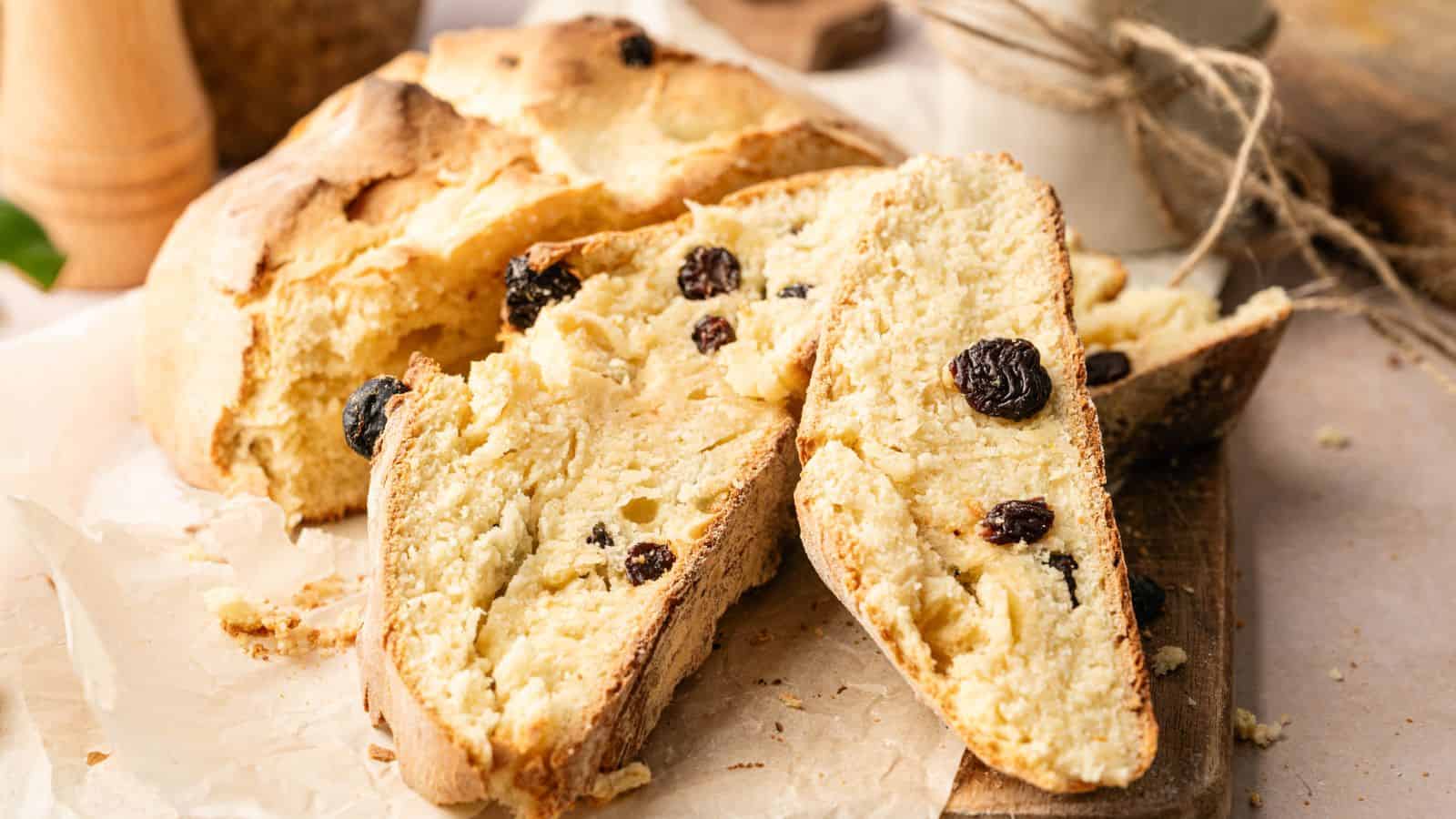 Sliced loaf of rustic bread with raisins on a wooden board and parchment paper.