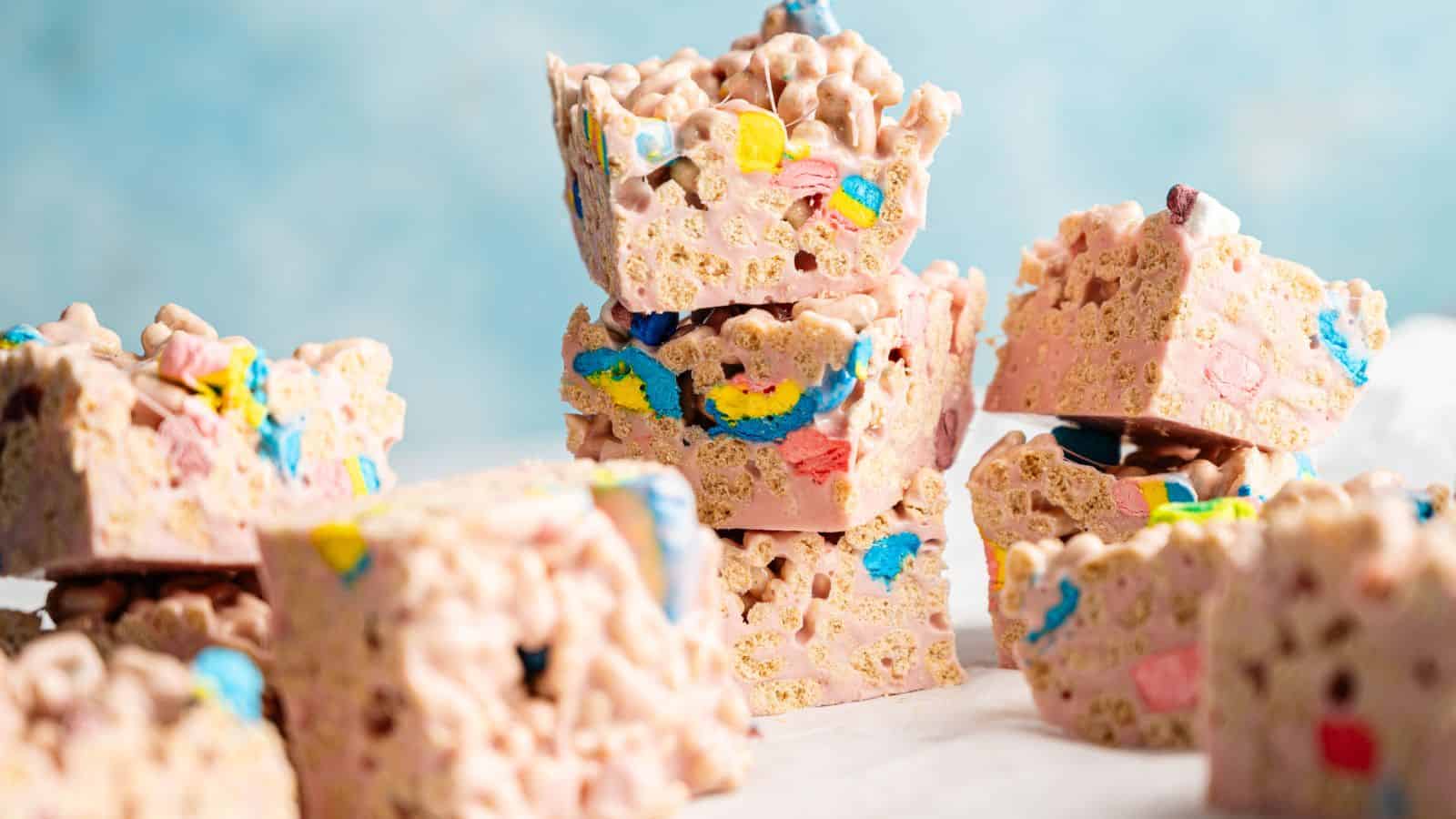 A close-up of stacked cereal treats made with colorful marshmallows and crispy cereal pieces, set against a light blue background.