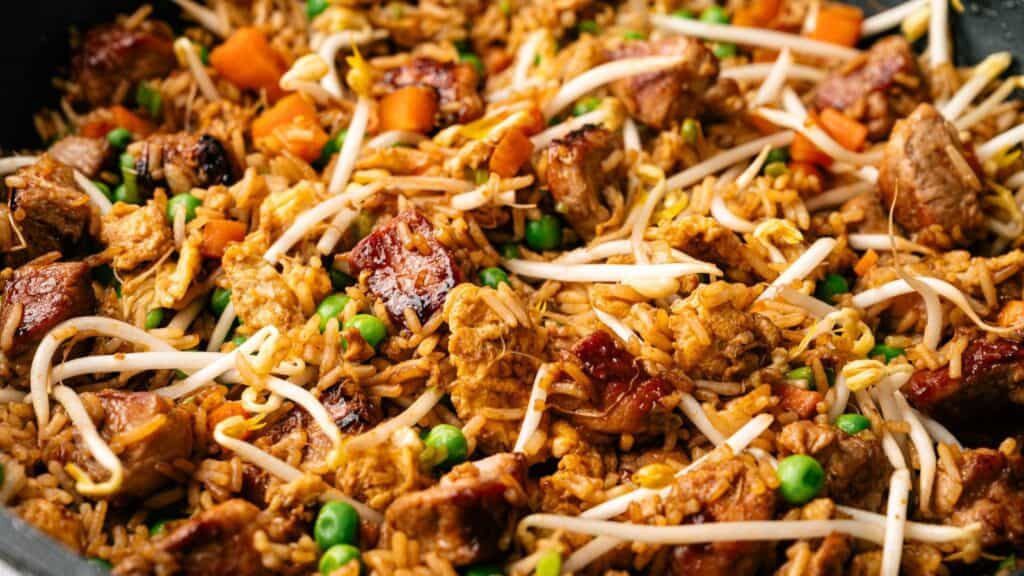 Close-up of fried rice with pieces of meat, peas, diced carrots, and bean sprouts.