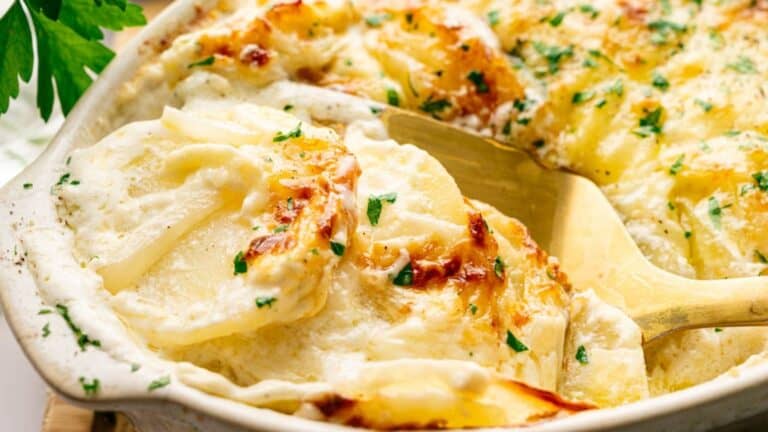 Close-up of a serving of creamy, cheesy scalloped potatoes garnished with chopped parsley in a white baking dish.