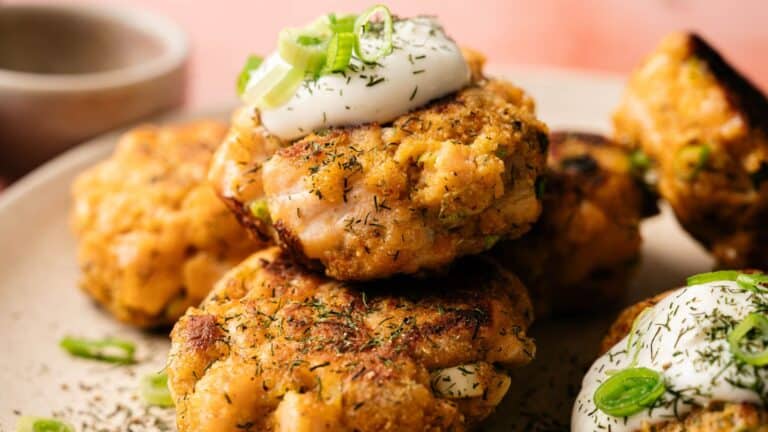 Close-up of golden-brown salmon patties topped with sour cream and chopped green onions, served on a plate.