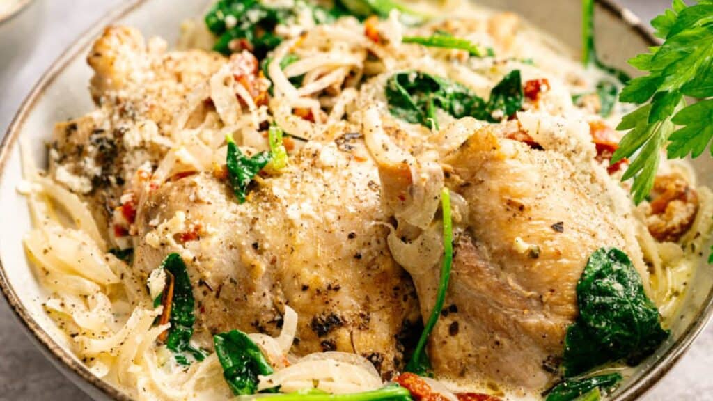 Cooked chicken thighs served with sautéed onions, spinach, sun-dried tomatoes, and a creamy sauce, garnished with black pepper.