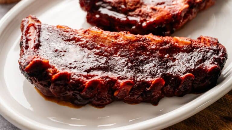 A close-up of a barbecued pork rib with a thick, glossy layer of barbecue sauce on a white plate.