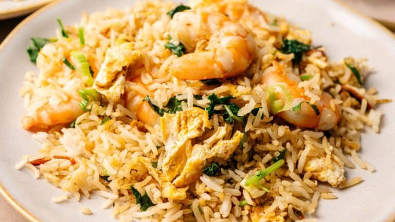 A plate of shrimp fried rice with pieces of scrambled egg, green onions, and leafy greens.