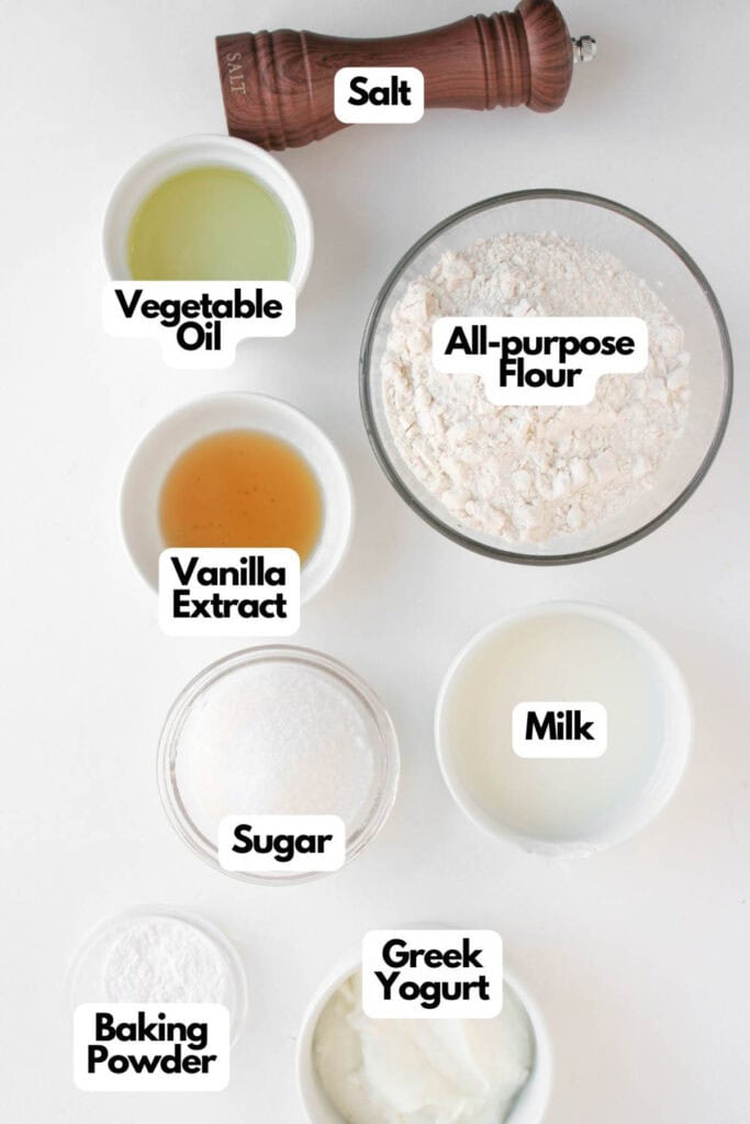 Ingredients for baking, including salt, vegetable oil, all-purpose flour, vanilla extract, milk, sugar, Greek yogurt, and baking powder, arranged on a white surface&mdash;perfect for making Muffin Pan Strawberry Shortcakes.