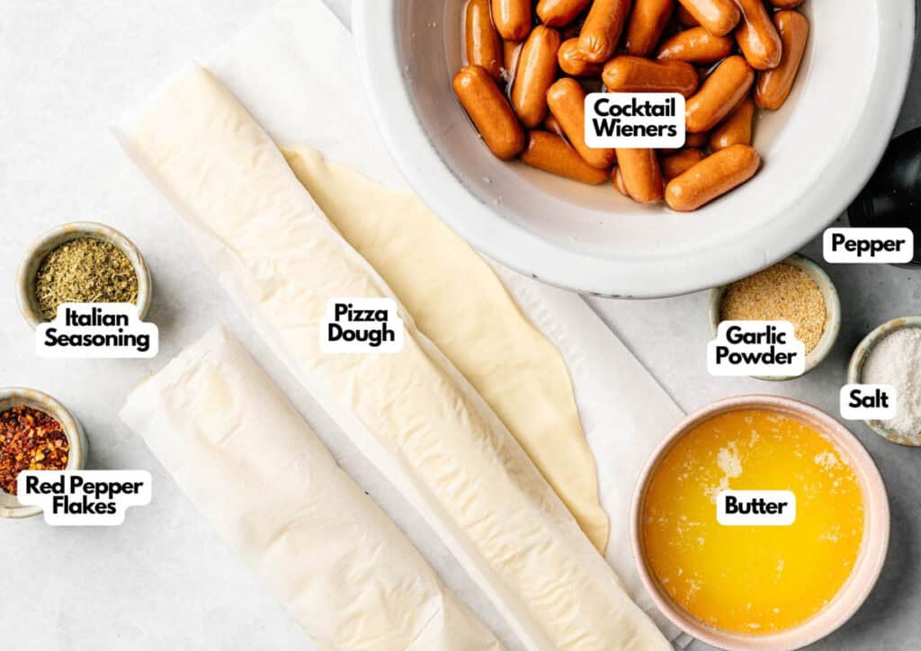 Pull-Apart Pigs in a Blanket ingredients&mdash;pizza dough, cocktail wieners, melted butter, Italian seasoning, red pepper flakes, garlic powder, pepper, and salt&mdash;are arranged on a kitchen counter.