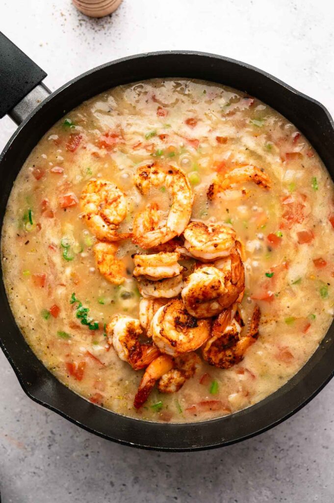 Cooked shrimp added to a simmering etouffee sauce in a cast iron pan.