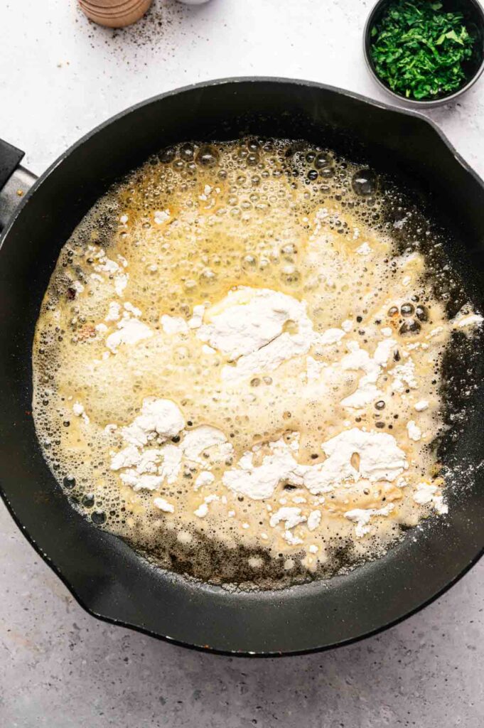 Butter and flour whisked together in a cast iron pan, forming the base of a roux.