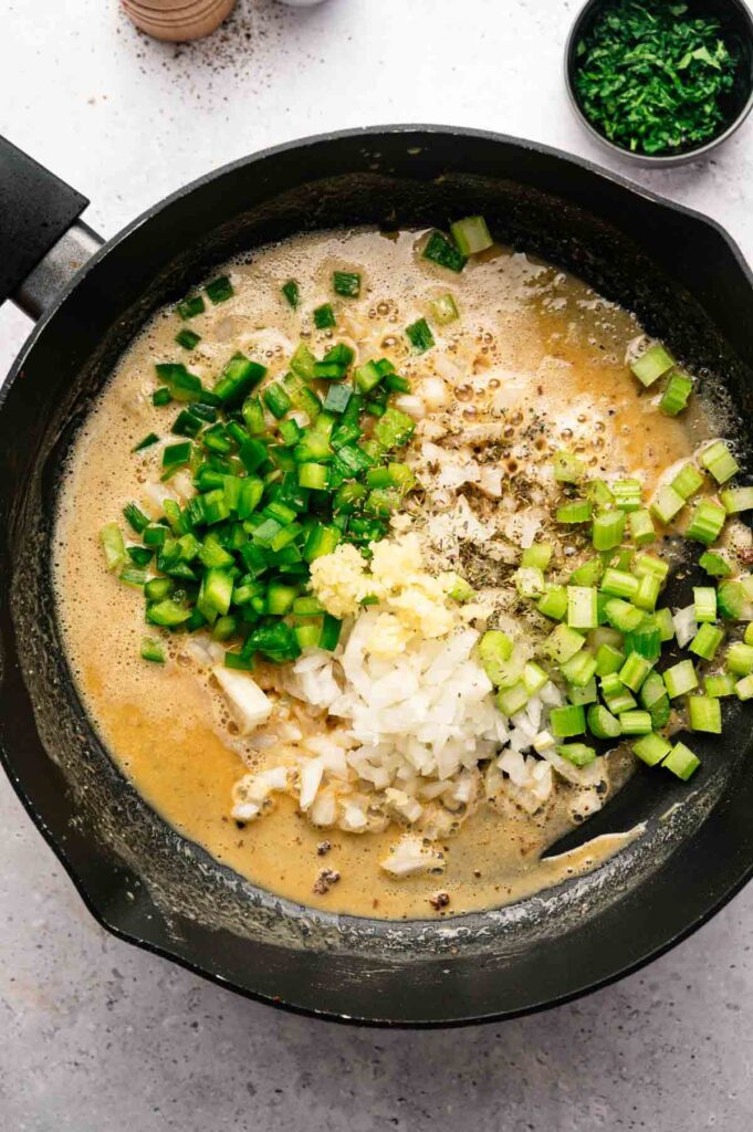 Chopped onion, bell pepper, celery, and garlic added to a roux in a cast iron pan.