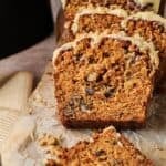 Sliced loaf of Air Fryer Carrot Cake with nuts, topped with a drizzle of white icing, displayed on parchment paper.