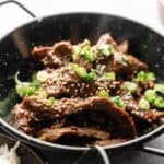 A black bowl filled with sliced Beef Bulgogi cooked in sauce, topped with sesame seeds and chopped green onions.