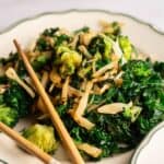 A plate of sautéed broccoli, kale, and onions inspired by Panda Express Super Greens, served with a pair of wooden chopsticks on the side.