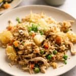 A plate of Pineapple Fried Rice with shredded chicken, sweet pineapple chunks, peas, carrots, and green onions.