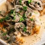 A plate of Slow Cooker Chicken Breast topped with creamy mushroom sauce and garnished with chopped parsley.