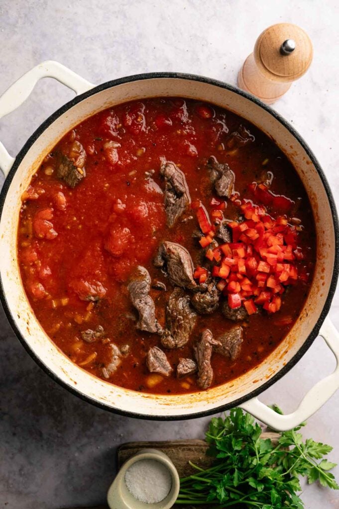 Browned beef, diced tomatoes, and red bell pepper simmering in a Dutch oven.