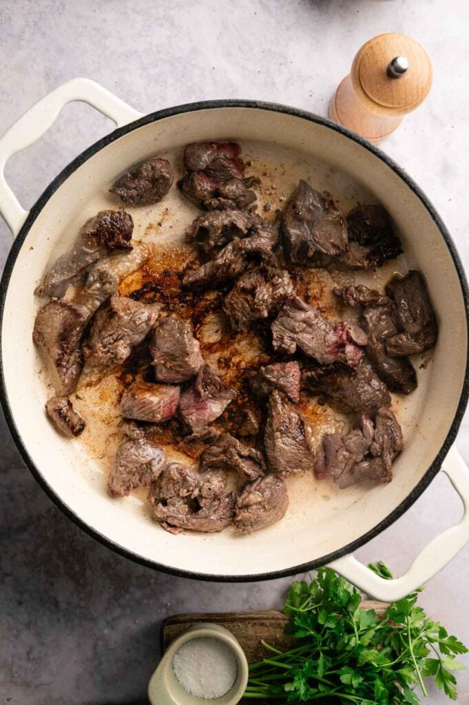 Cubes of beef browning in batches in a white Dutch oven.