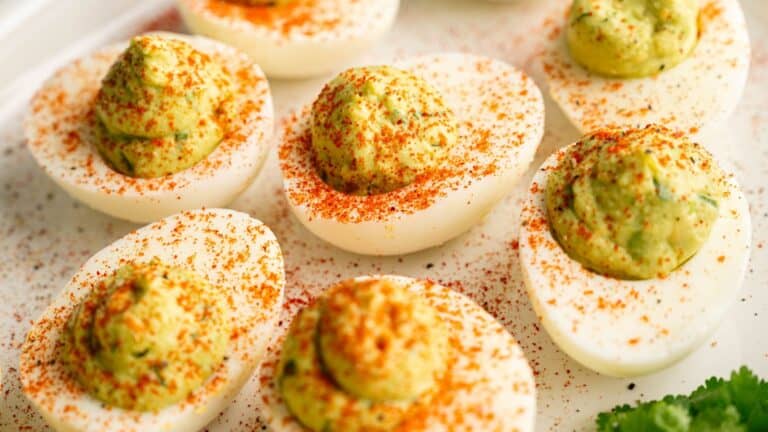 Close-up of deviled eggs topped with paprika, arranged on a white plate.