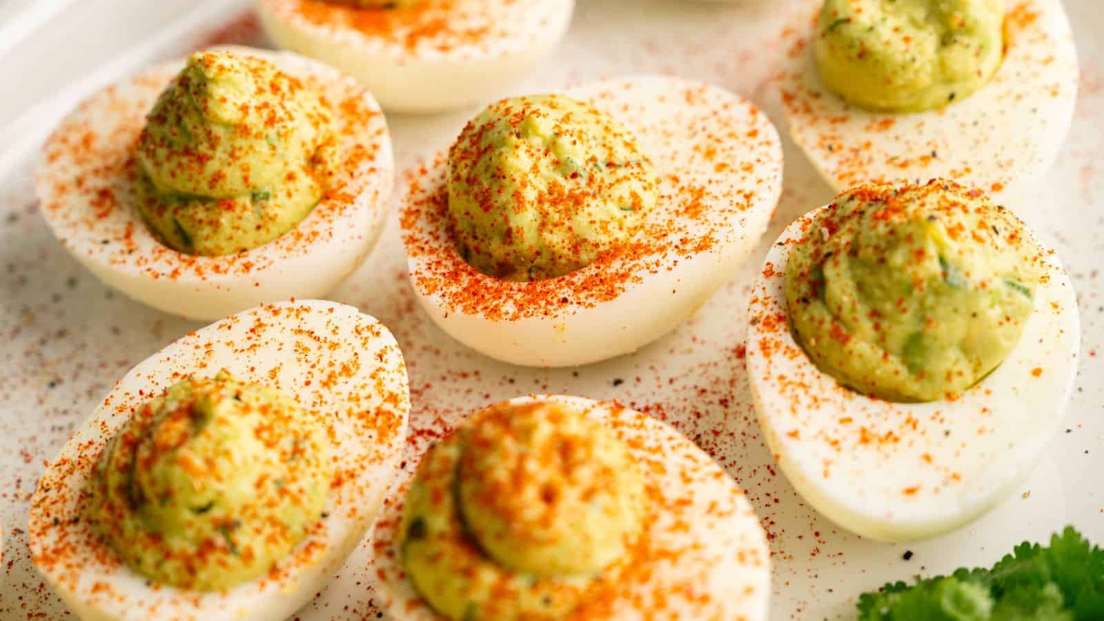 A close-up of deviled eggs with a creamy green filling, topped with a sprinkle of red paprika, arranged on a white plate.