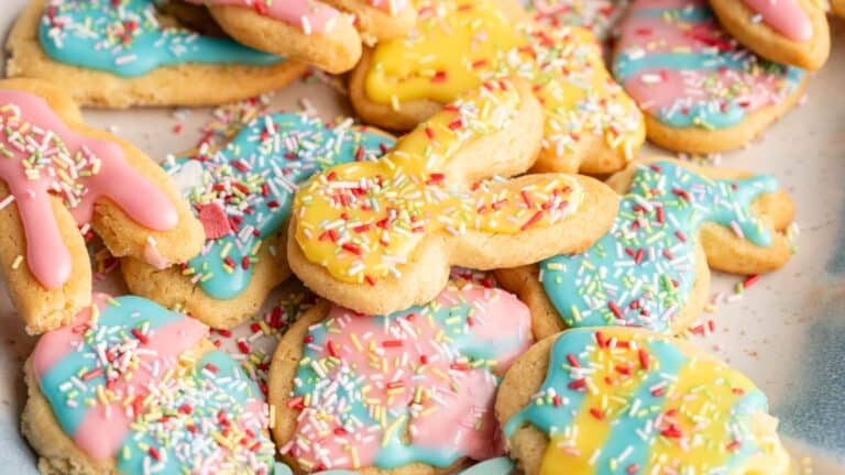 A pile of sugar cookies shaped like bunnies and eggs, decorated with pastel pink, blue, and yellow icing and multicolored sprinkles.