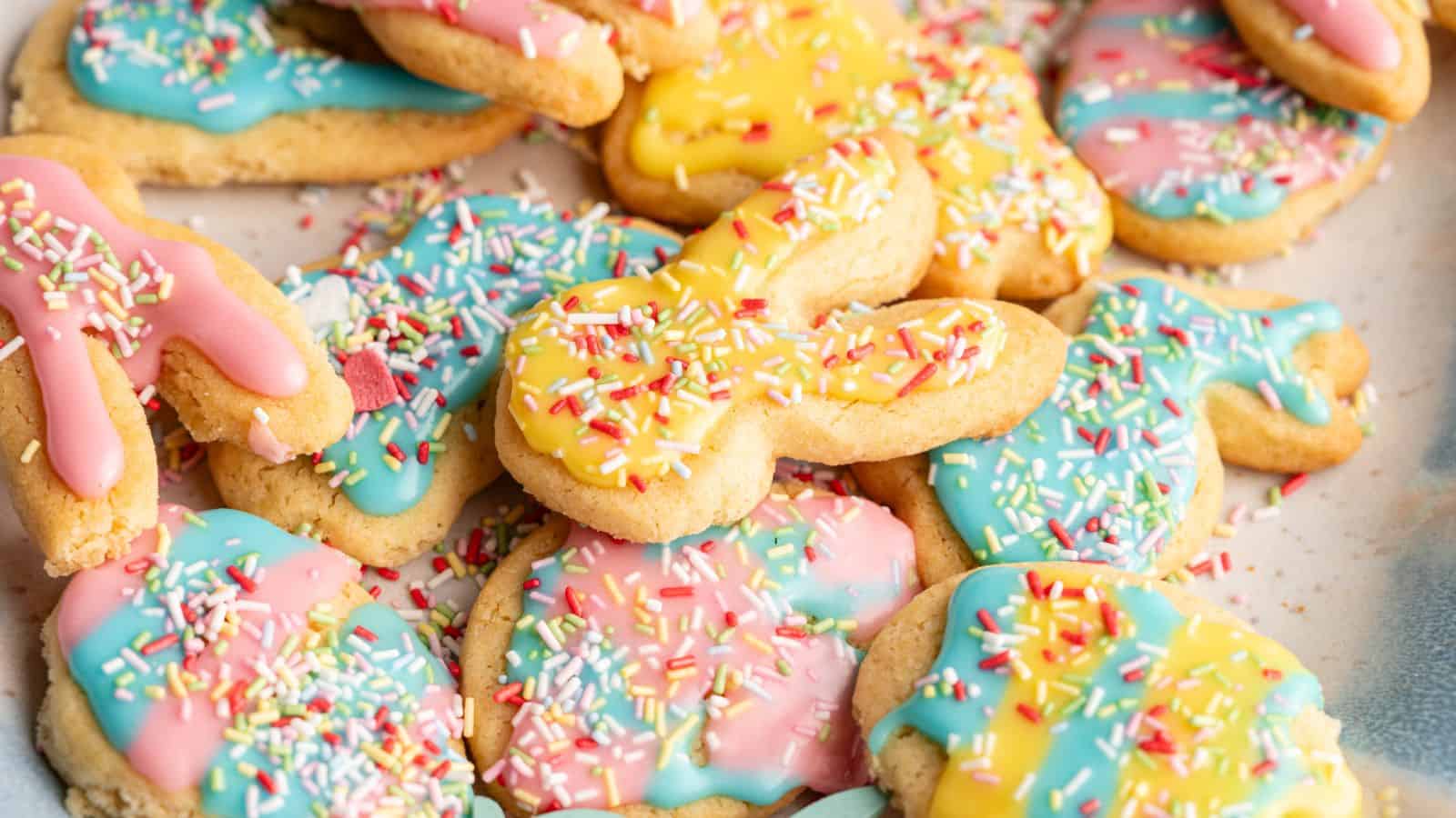 A pile of sugar cookies shaped like bunnies and other forms, decorated with pastel pink, yellow, and blue icing and topped with colorful sprinkles.