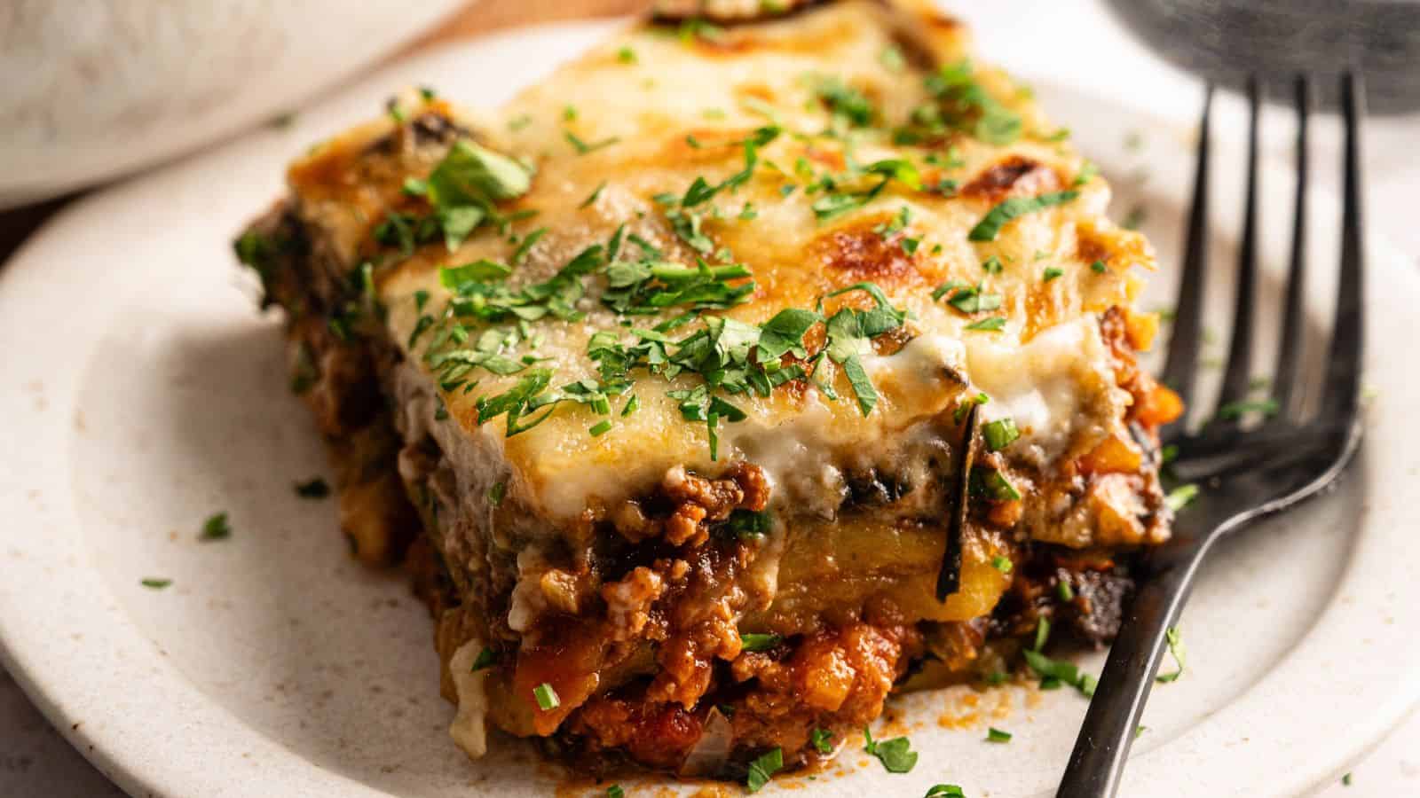 A bowl of white rice topped with meatballs, cherry tomatoes, black olives, sliced red onion, cucumber, and a dollop of white sauce, garnished with fresh herbs.