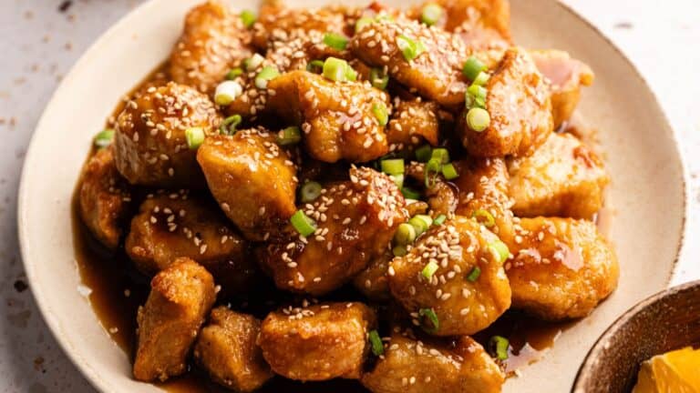 A plate of glazed chicken pieces garnished with sesame seeds and chopped green onions.