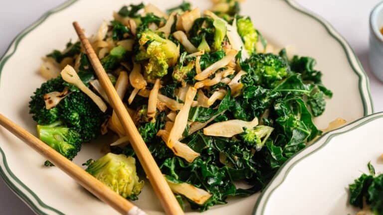 A plate of stir-fried broccoli, kale, and onions, served with chopsticks on the side.