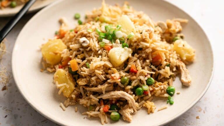 A plate of fried rice with peas, carrots, pineapple chunks, shredded chicken, and chopped green onions.