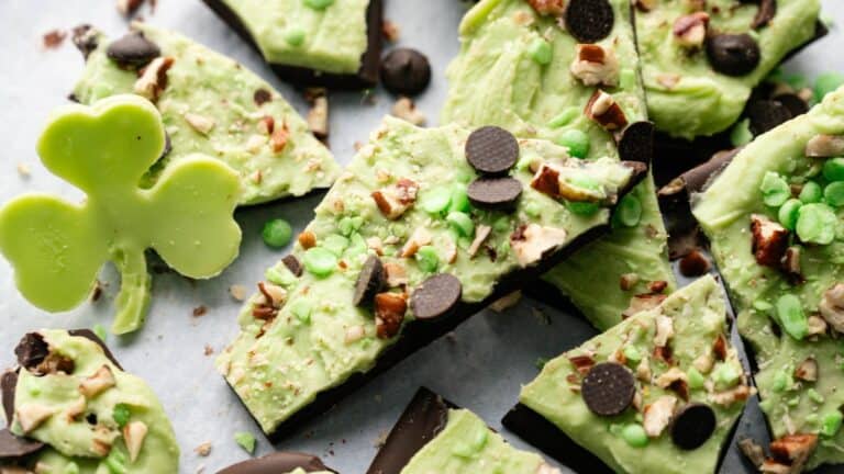 Pieces of chocolate bark topped with green mint layer, chocolate chips, nuts, and green candy, next to a shamrock-shaped green confection.