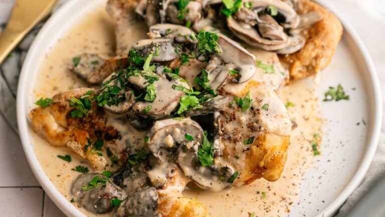 Chicken breasts topped with creamy mushroom sauce and garnished with chopped parsley, served on a white plate.