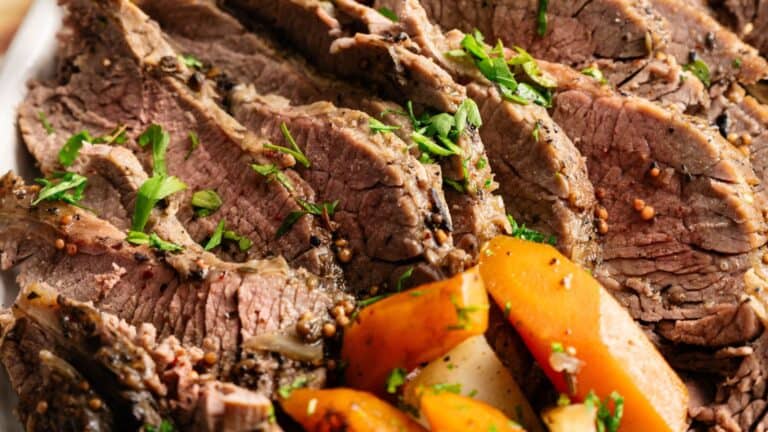 Sliced roast beef garnished with chopped parsley, served with cooked carrots and potatoes.