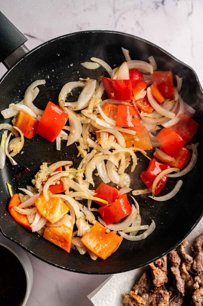 Sliced red bell pepper and onion caramelizing in a black skillet.