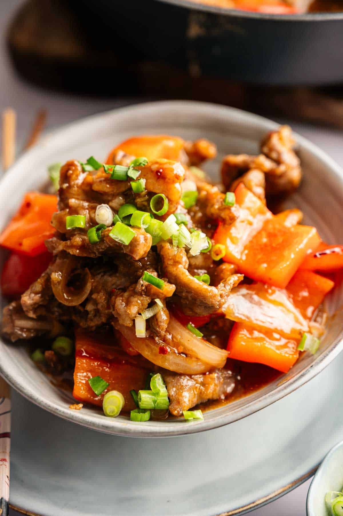 A bowl of stir-fried beef inspired by Panda Express Beijing Beef, with red bell peppers, onions, and sliced green onions on top.
