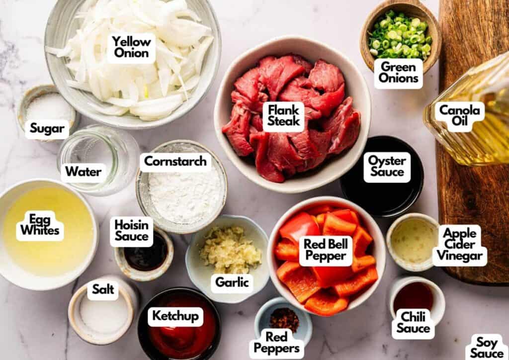 Various labeled ingredients for a stir-fry recipe, inspired by Panda Express Beijing Beef, including sliced flank steak, onions, red bell pepper, sauces, spices, oil, and seasonings arranged on a white surface.
