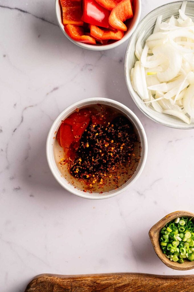 Small bowls of red pepper, sliced onion, and a spicy sauce mixture with chili flakes and ketchup.